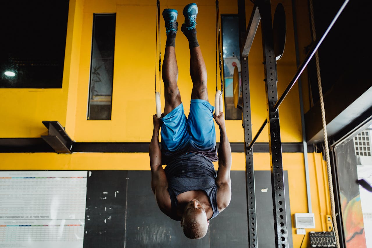 Male athlete doing gymnastics on rings indoors, showcasing strength and fitness in a gym setting.